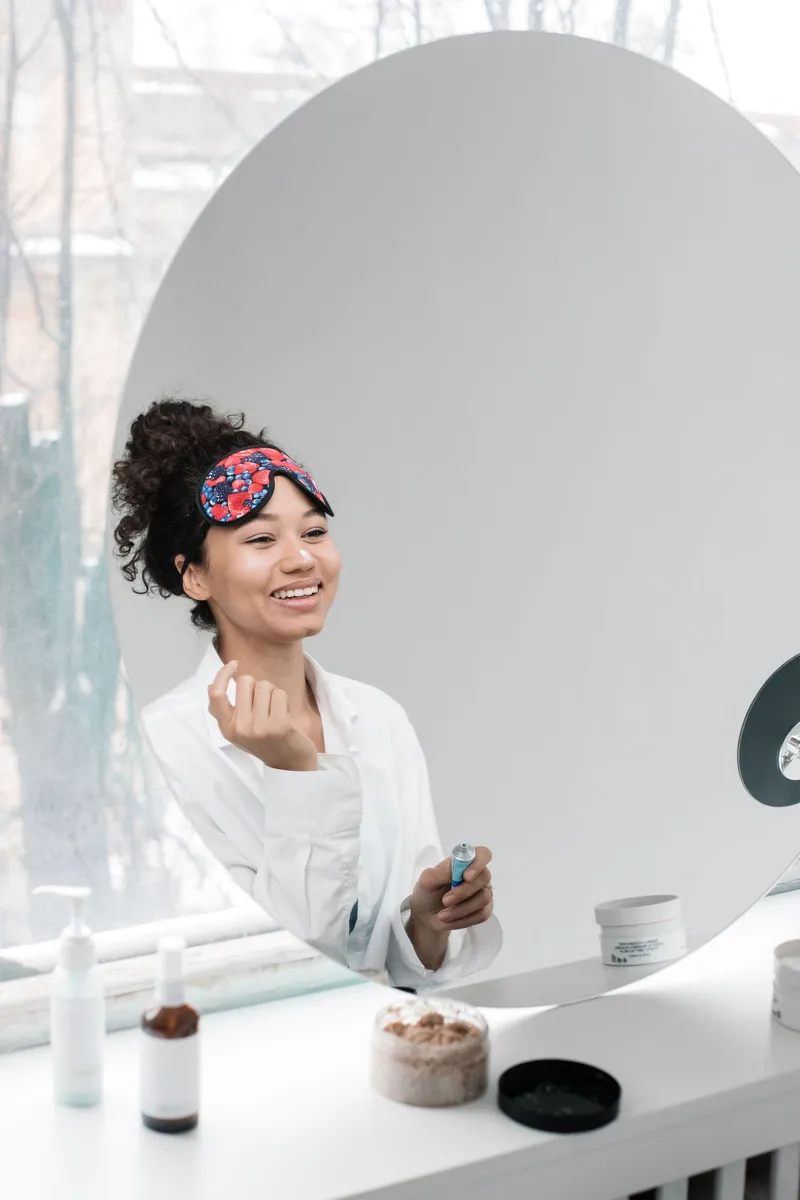 Mujer sonriente aplicándose su rutina de cuidado facial frente al espejo