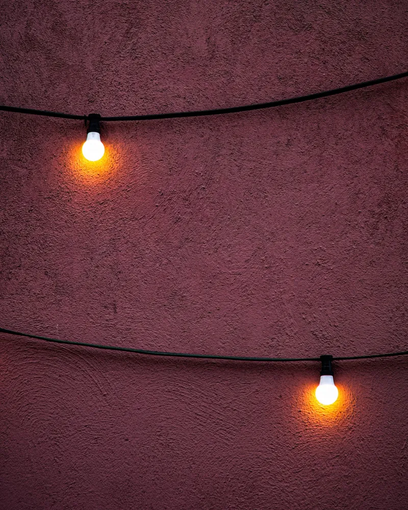 Bombillas colgantes de luz cálida frente a una pared roja.