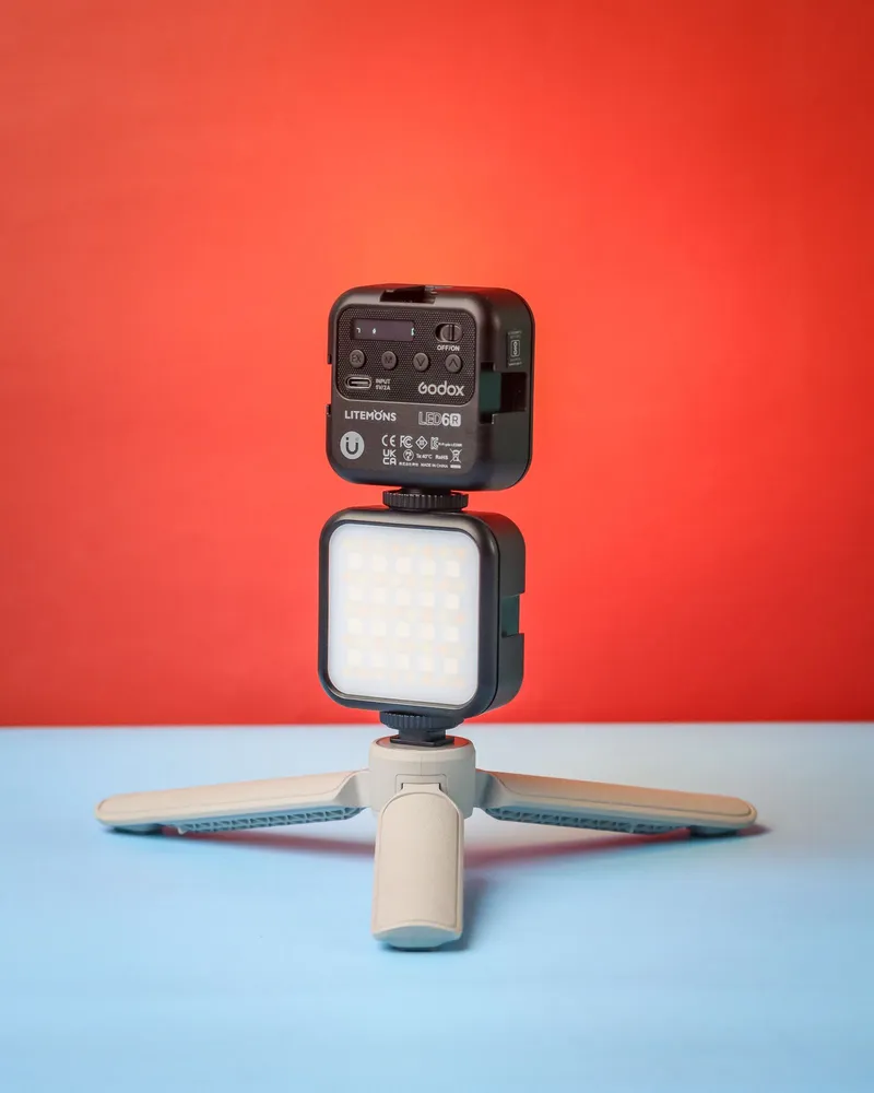 Foco LED portátil montado en trípode sobre un fondo rojo.