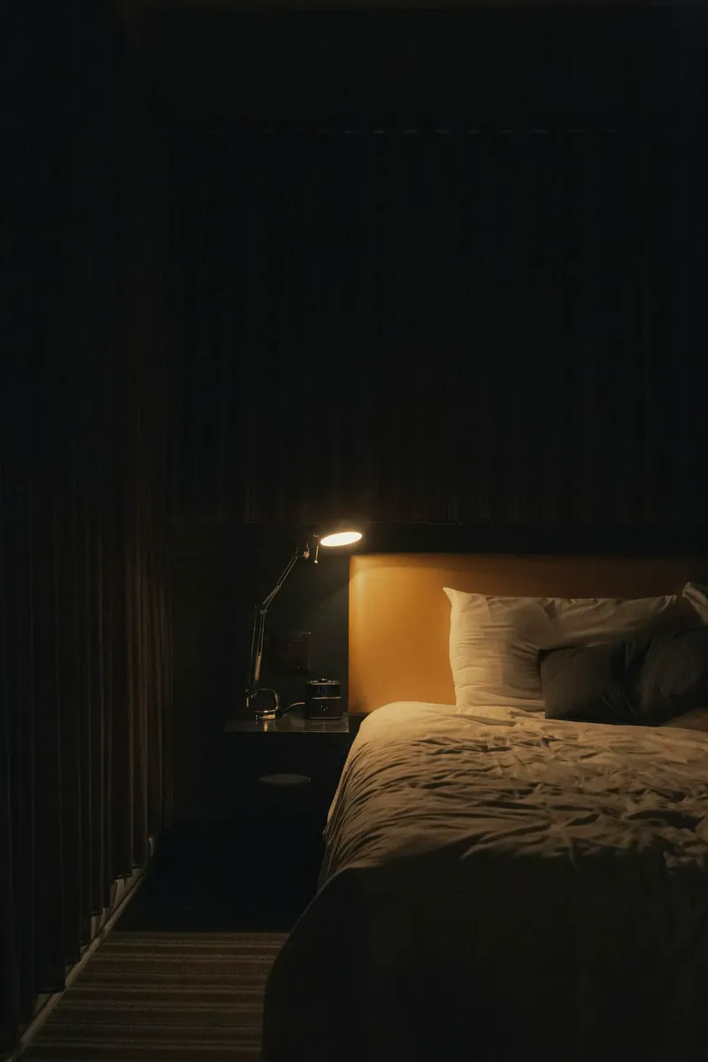Lámpara de mesita encendida con luz cálida junto a la cama en un dormitorio en penumbra