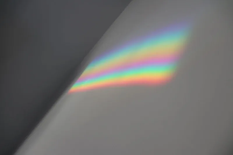 Refracción de luz en colores del arcoíris proyectada sobre una pared gris.